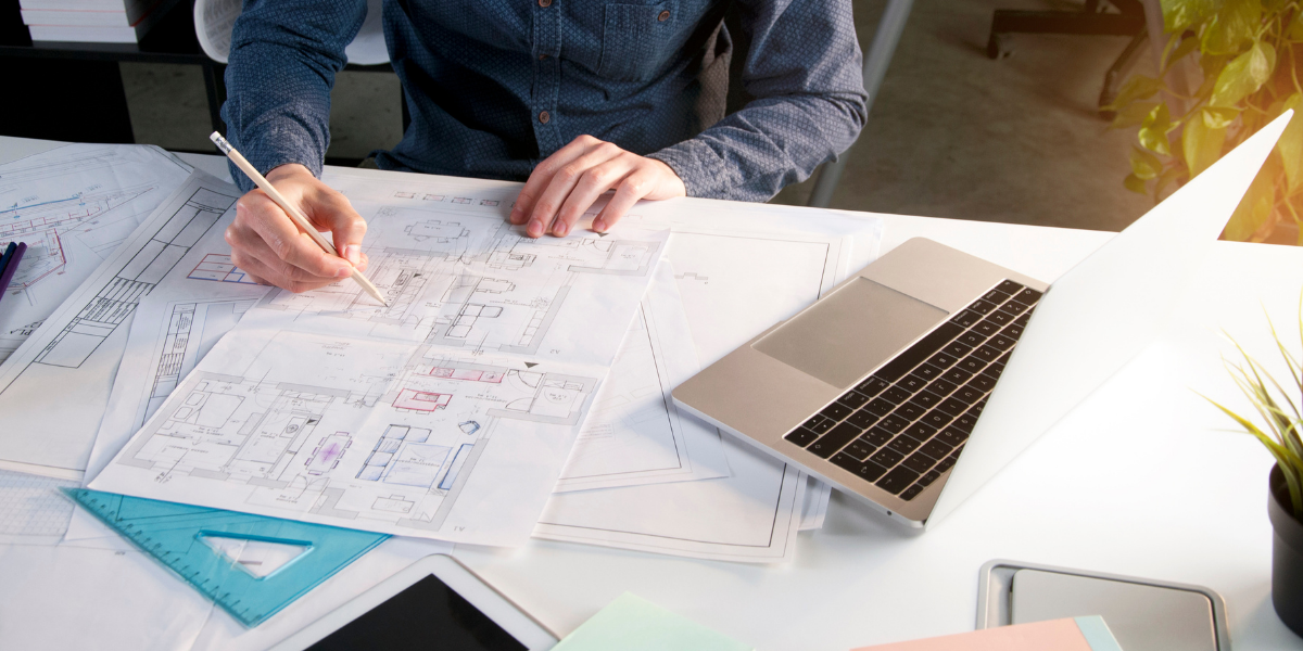 Someone working on blueprints with laptop on desk